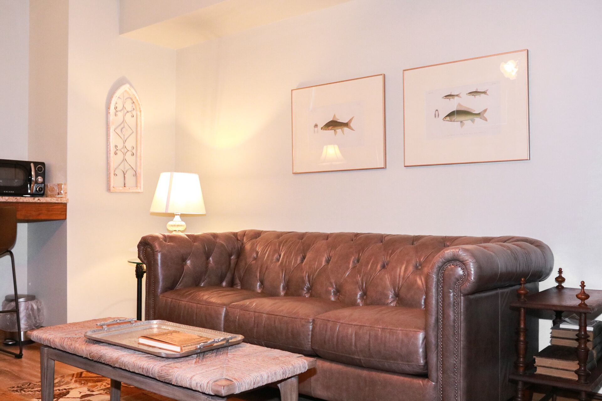 Un salon avec un canapé en cuir marron, une petite table sur laquelle se trouve un plateau, une lampe et deux tableaux représentant des poissons, accrochés au mur.