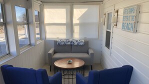 Une pièce chaleureuse avec un canapé gris, deux fauteuils bleus, une petite table en bois et une fenêtre donnant sur un beau paysage.