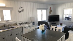 Une cuisine moderne avec des meubles blancs, une cuisinière à gaz et un coin repas comprenant une table en bois foncé et des chaises blanches.