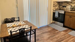 Zona pranzo con tavolo apparecchiato per due, cucina con elettrodomestici moderni e una porta vetrata scorrevole che dà su un balcone.