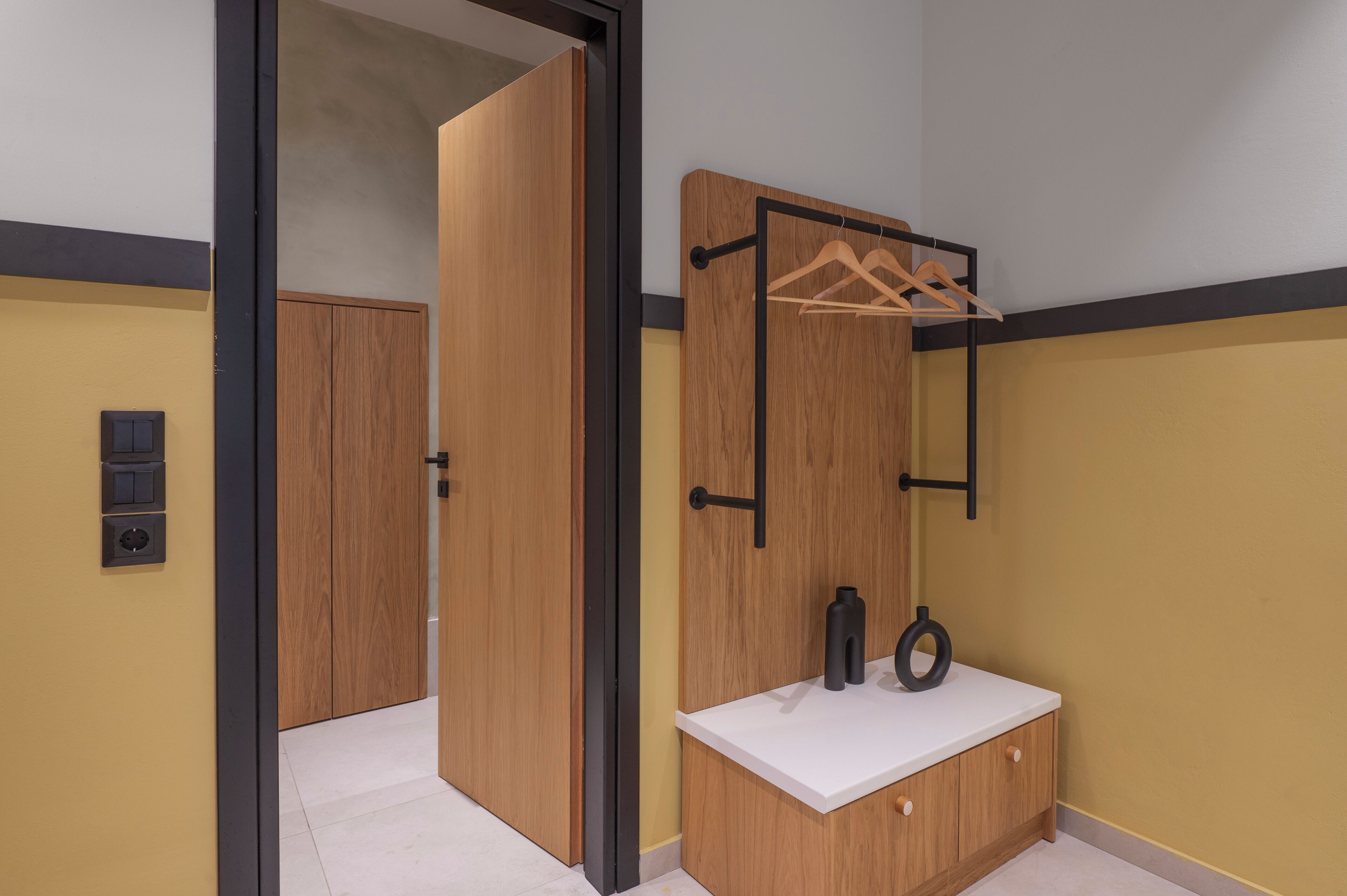 A room with a wooden wardrobe, a white countertop with a mirror, and a hanging rack.