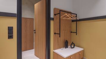 A room with a wooden wardrobe, a white countertop with a mirror, and a hanging rack.