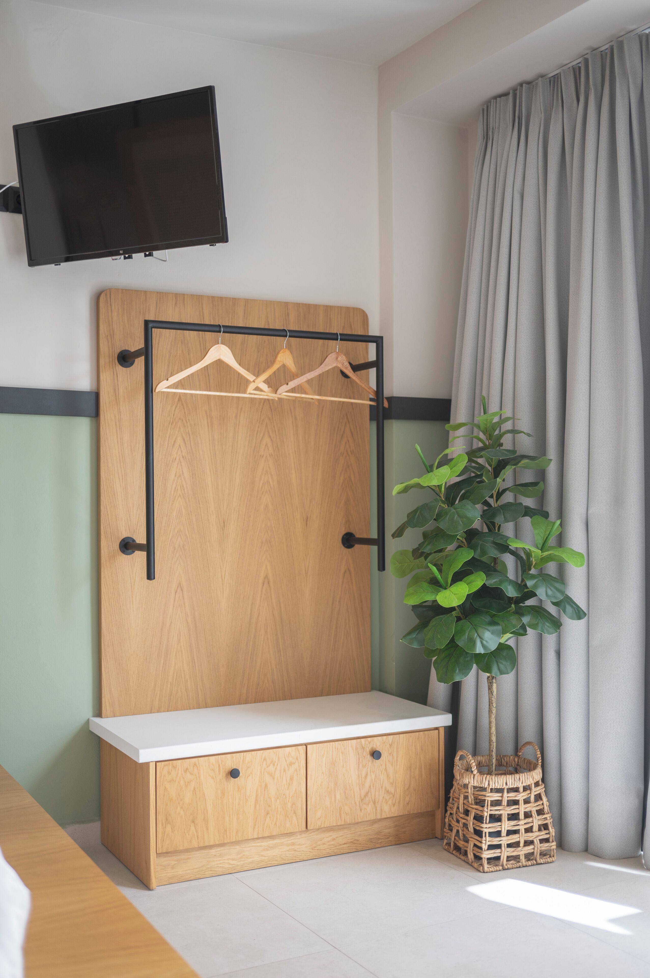 A room with a wooden cabinet, a mounted TV, a plant, and a window with curtains.