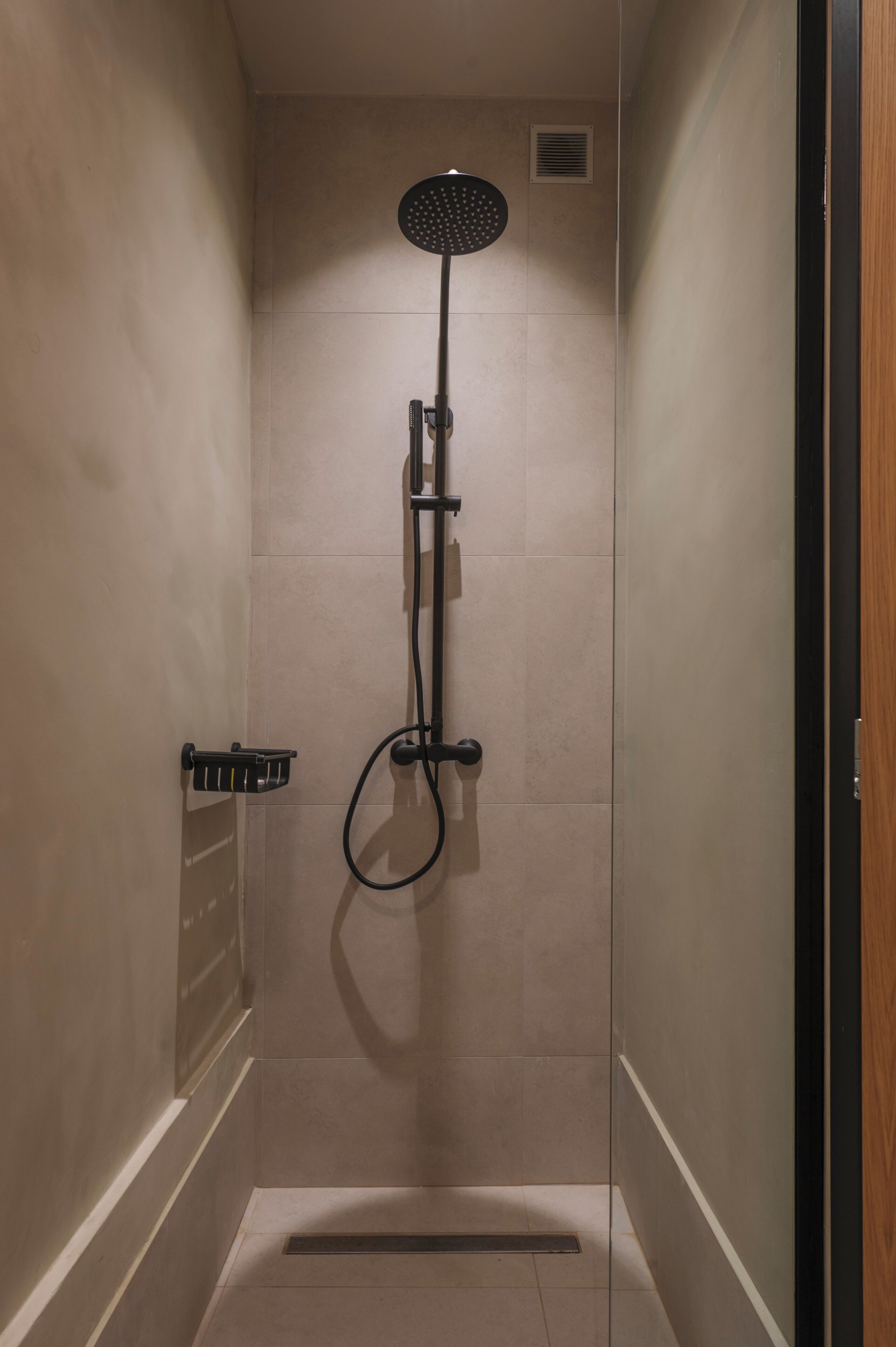 A small, enclosed shower area with a handheld showerhead and a wall-mounted control panel.
