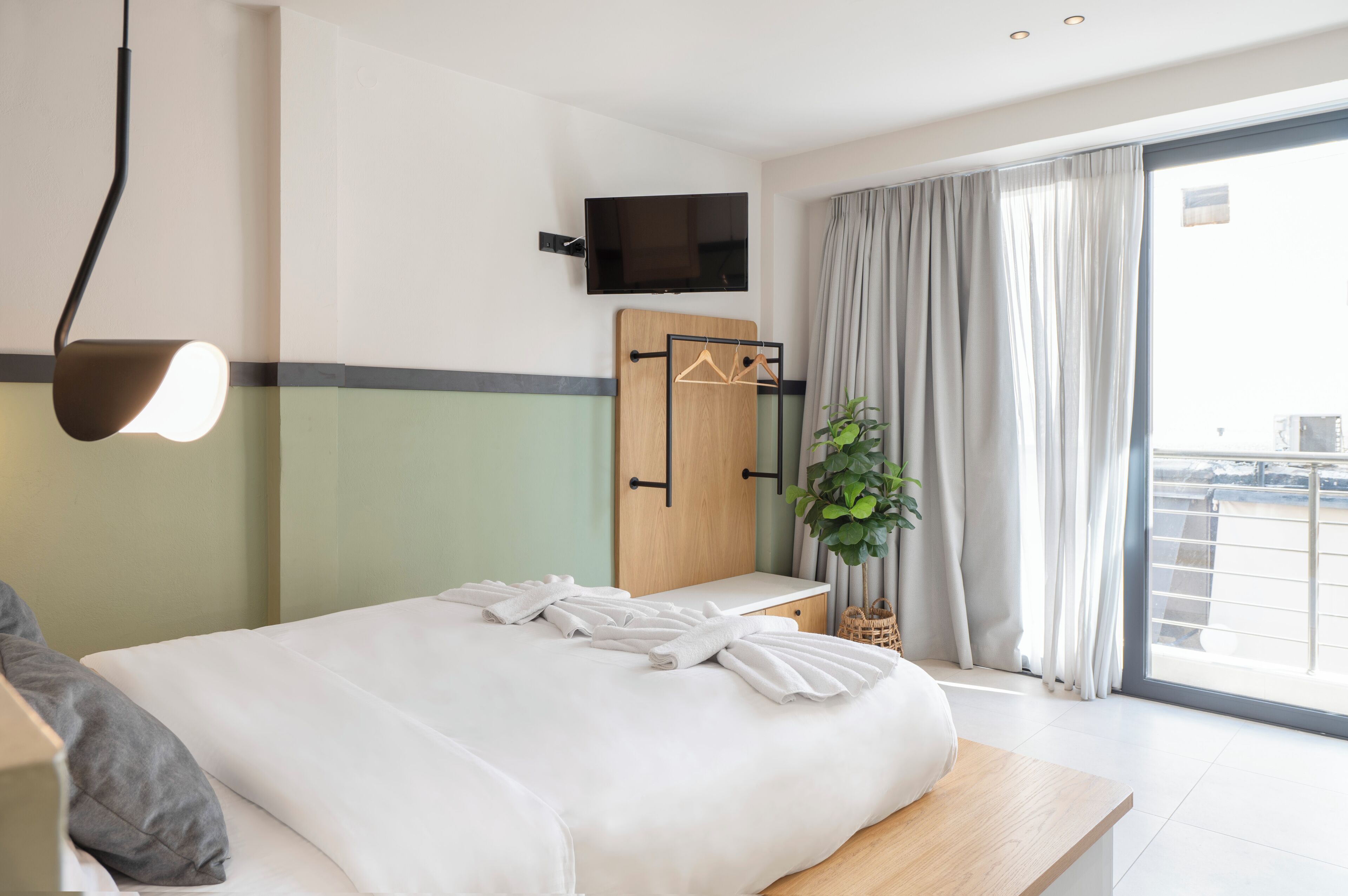 A modern hotel room with a bed, bedside table, TV, and a balcony with curtains.