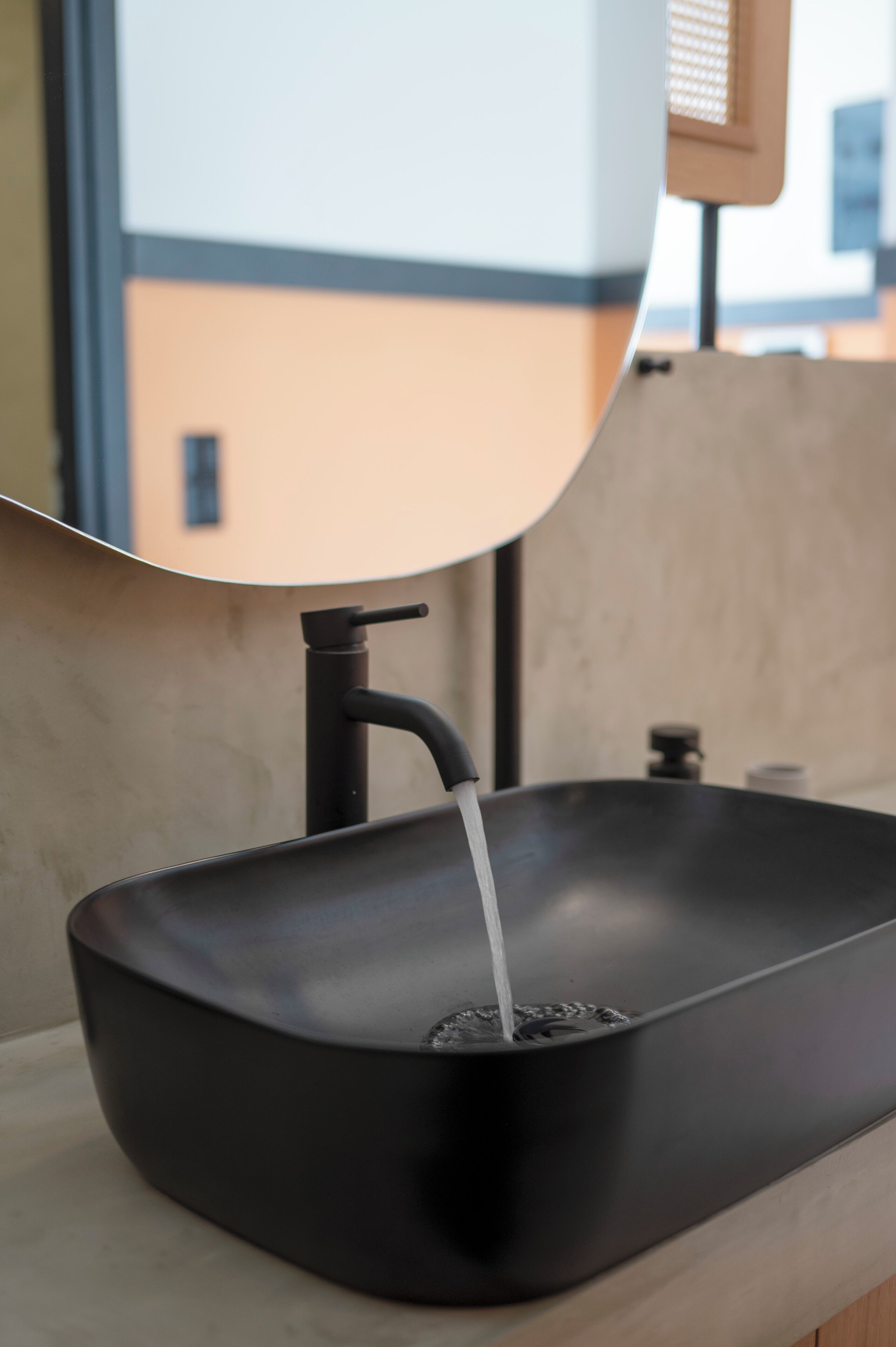 A black rectangular sink with a faucet, water running from it, and a mirror reflecting a building outside.