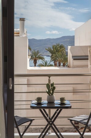 A balcony with a table and chairs, a potted plant, and a view of palm trees and mountains. - Casa di Cornaro (Sitia)