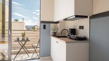 A compact kitchen with a sliding glass door leading to a balcony, a small table with a plant, and a coffee maker.