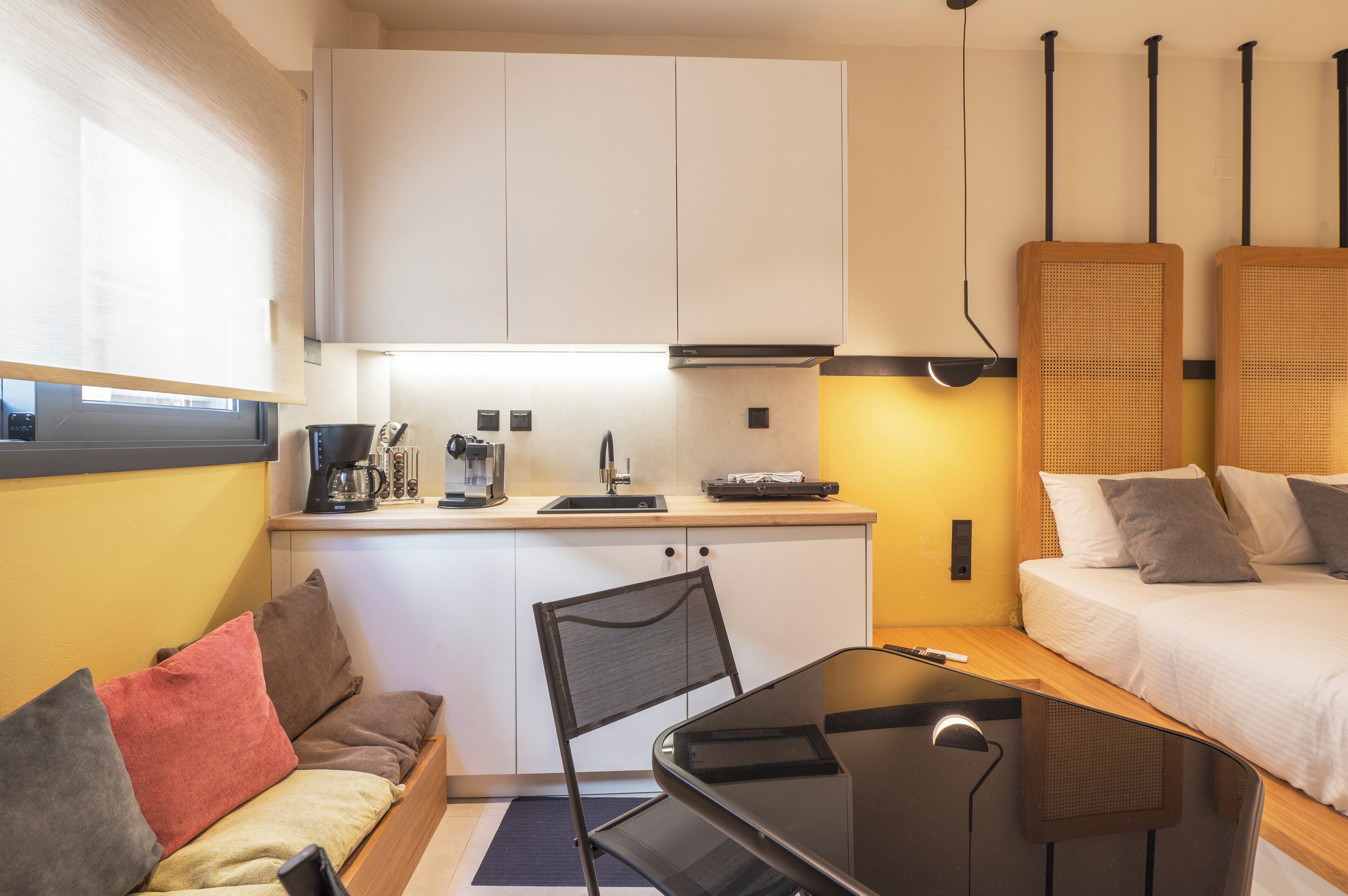 A compact hotel room with a kitchenette, a bed, a small sofa, and a dining table.