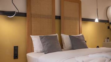 A neatly made bed with white linens and two grey pillows, a wooden headboard, a bedside table with a lamp, and a wall-mounted light fixture.