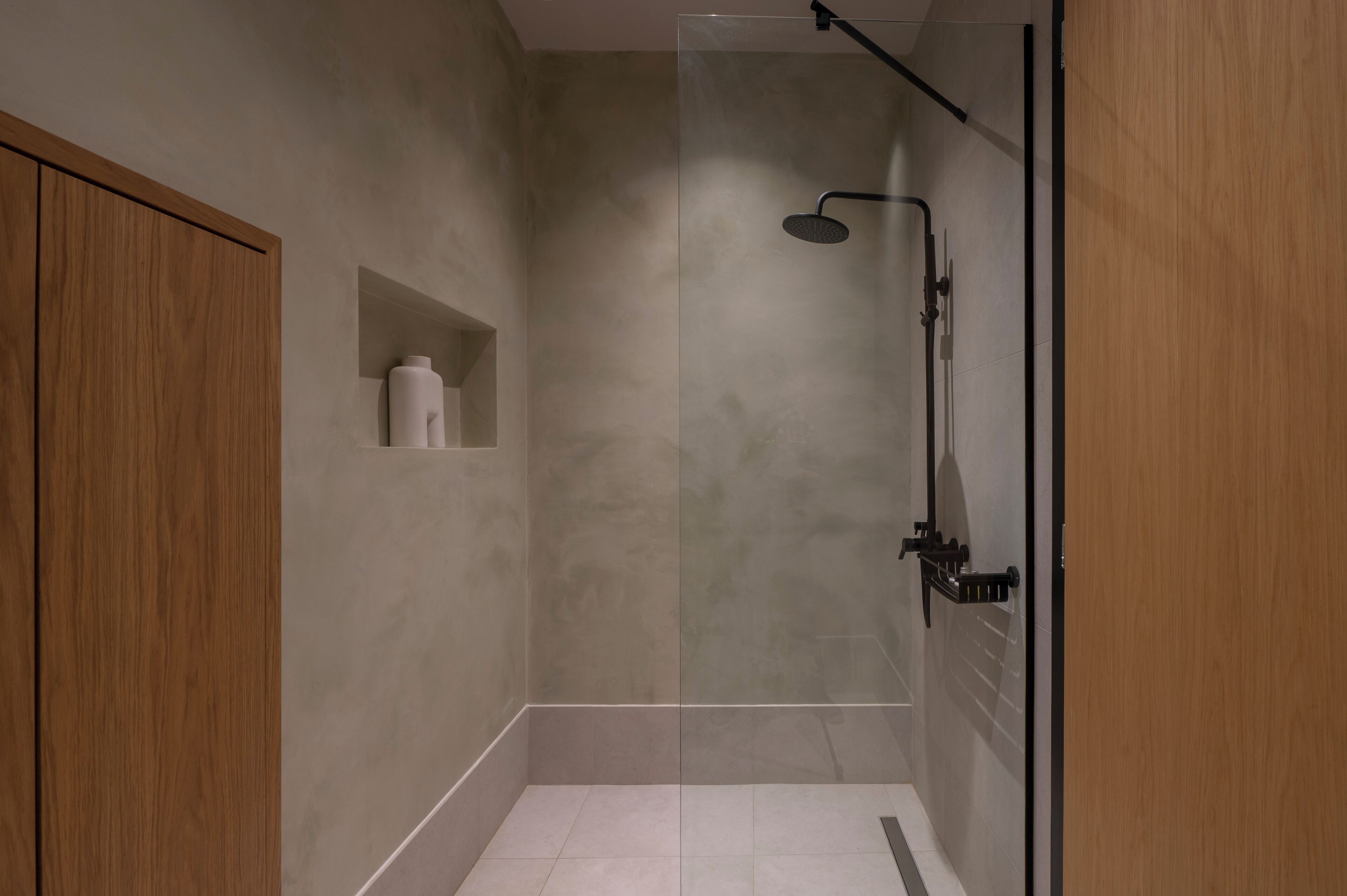 A modern shower area with a glass door, a wooden cabinet, and a small shelf with toiletries.