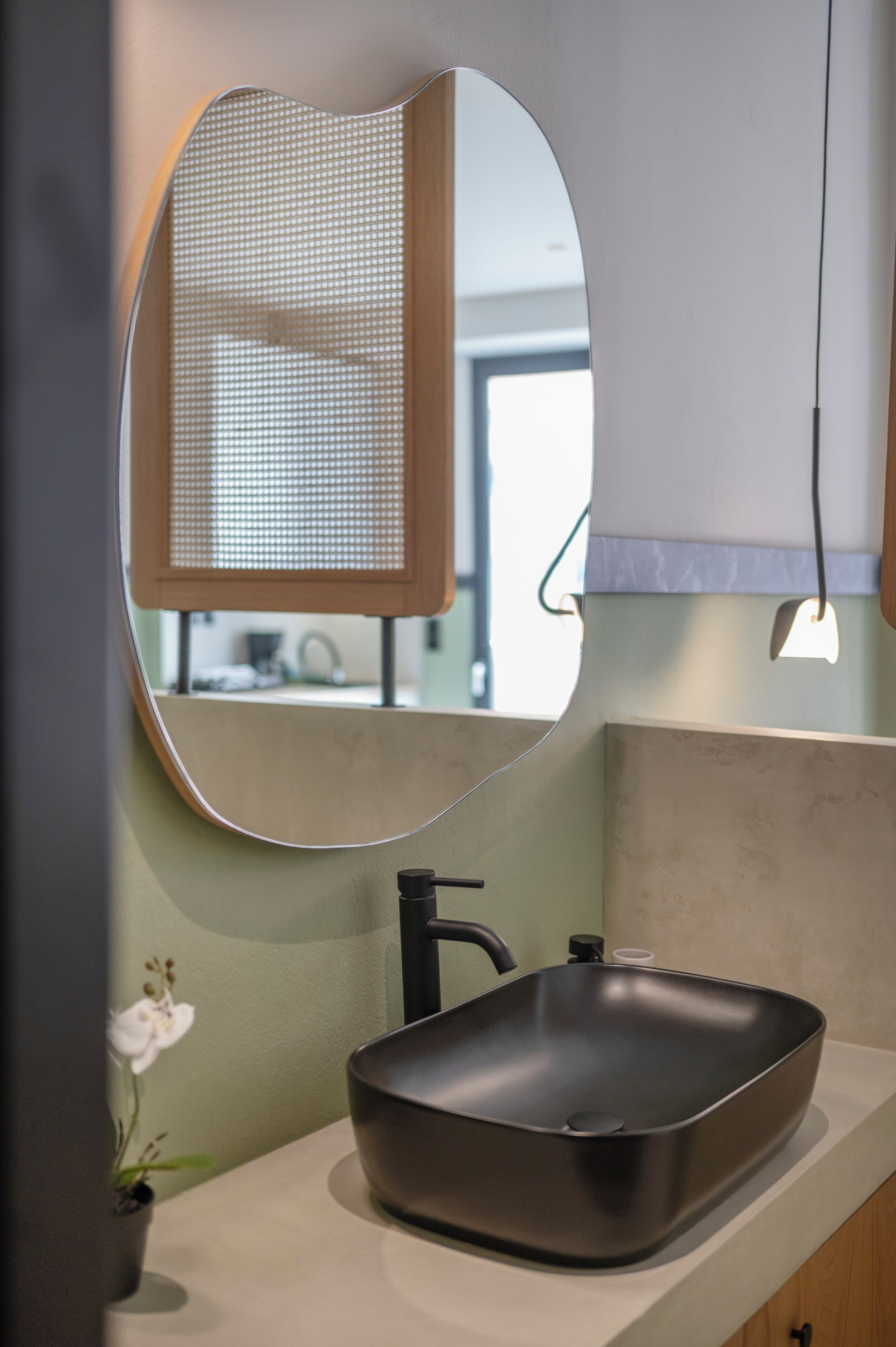 Une salle de bain moderne avec un lavabo rectangulaire, un miroir rond et une petite orchidée en pot.