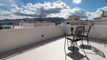 A rooftop terrace with a chair and table, overlooking a cityscape and mountains.