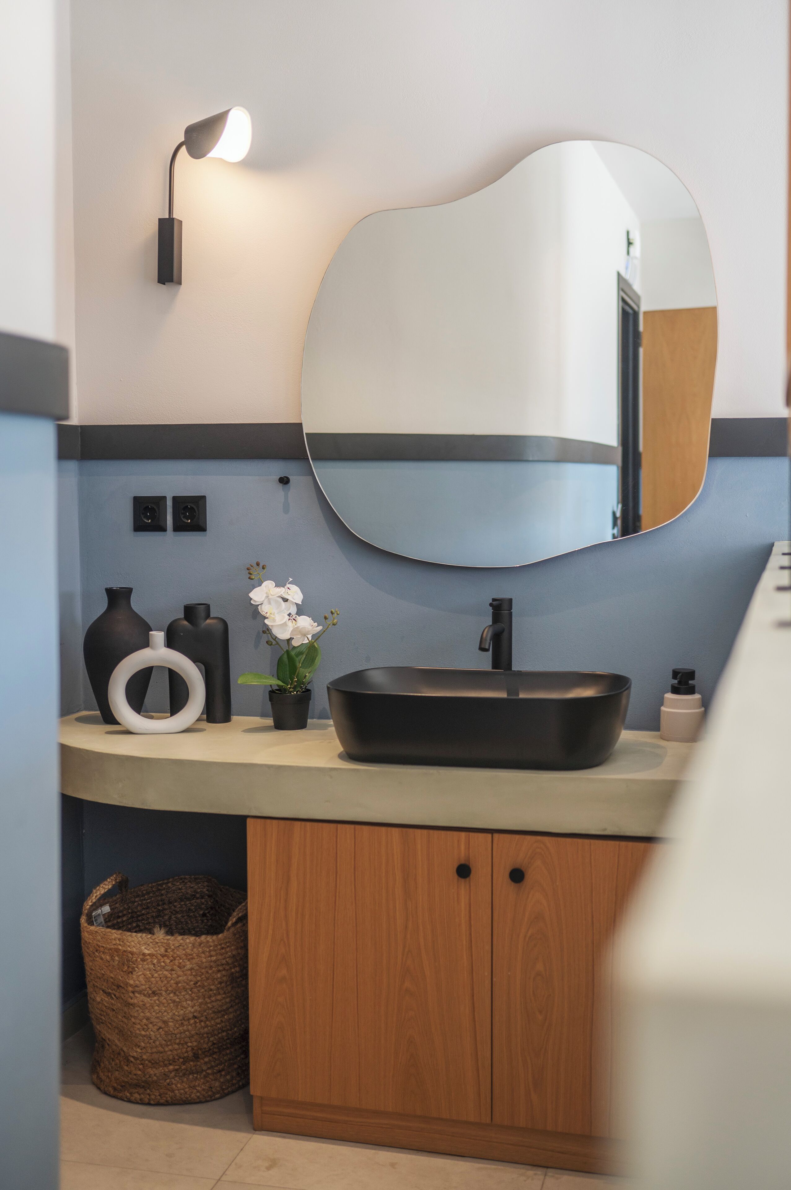 A bathroom with a modern sink, a round mirror, and a wall-mounted light.