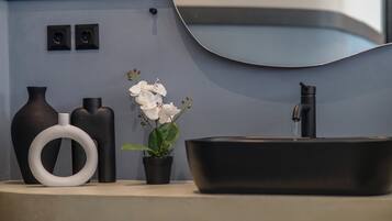 Baño con un lavamanos negro, un florero blanco, una orquídea en maceta y dos luces negras fijadas a la pared.