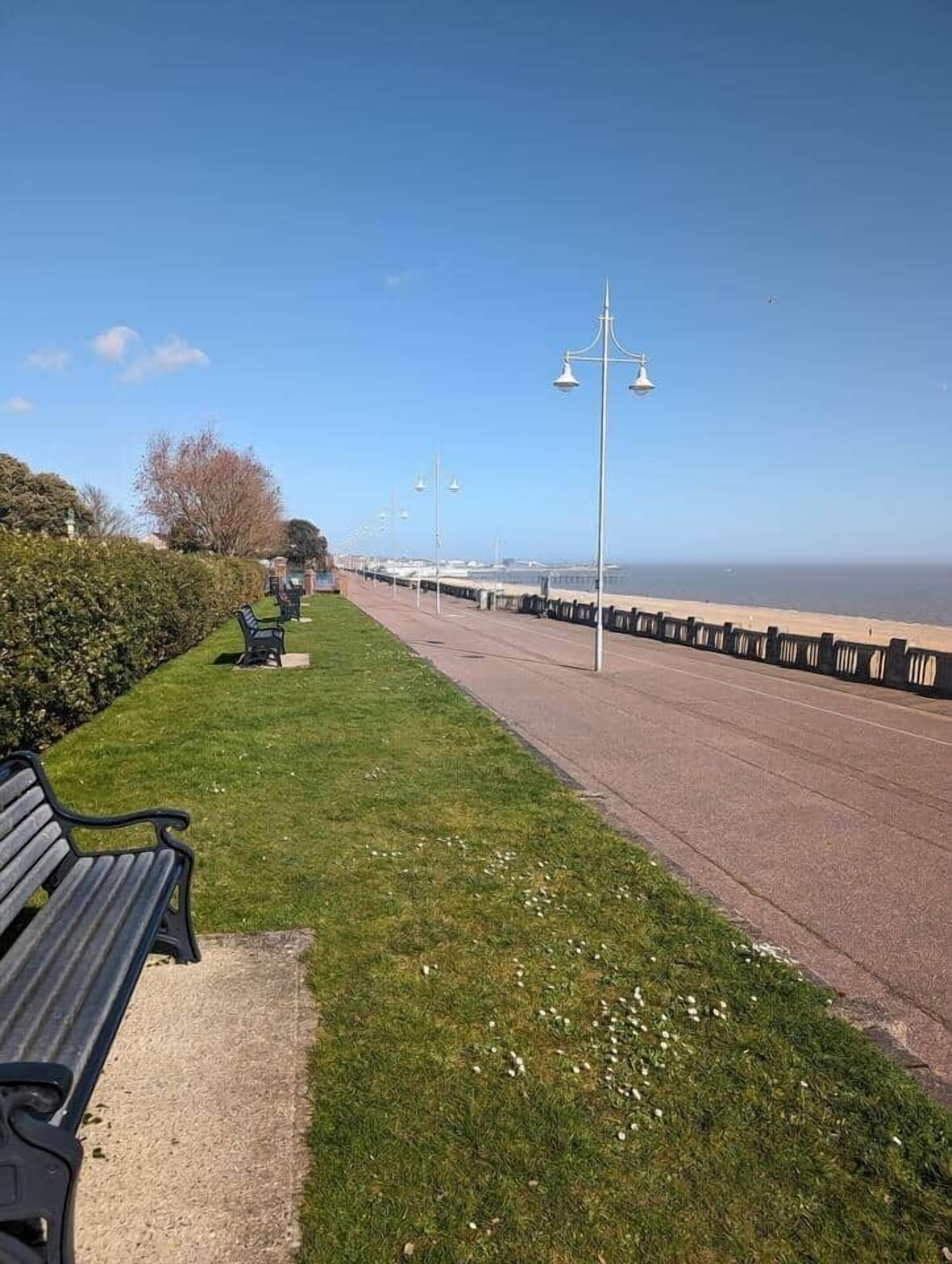 A coastal promenade with benches, a clear sky, and a view of the sea.