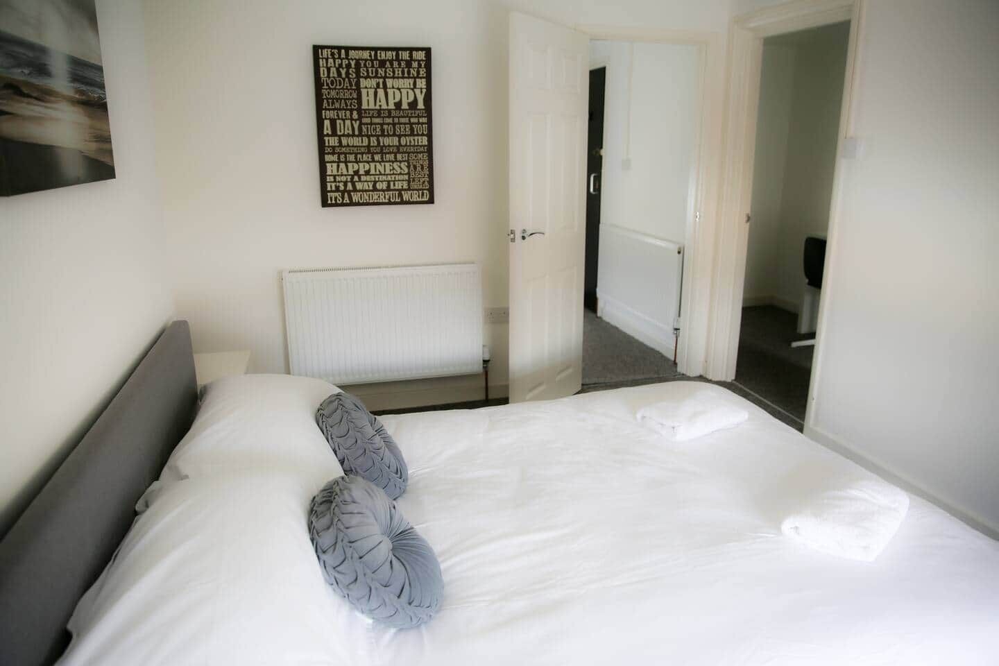 A hotel room with a neatly made bed, a radiator, and a motivational quote on the wall.
