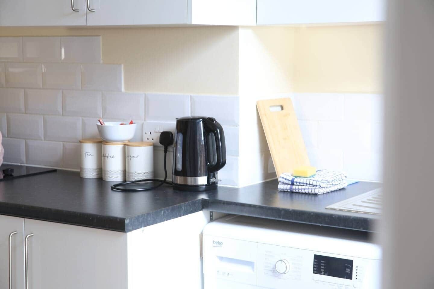 A kitchen with white cabinets, a black kettle, and a dish rack.