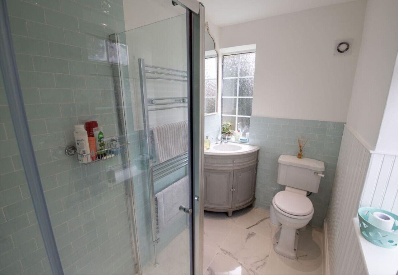 A bathroom with a glass shower enclosure, a white toilet, a sink with a mirror, and a window.