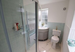 Een badkamer met een glazen douchecabine, toilet in het wit, een wastafel met spiegel, en een raam.