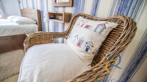Een rieten stoel met een kussen met architecturale patronen, een bed met wit beddengoed, en een gestreepte muur op de achtergrond.
