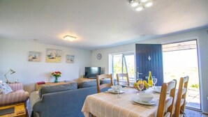 Een woonkamer met een bank, een eettafel gedekt met borden, glazen en een fles, en een televisie op een meubel.