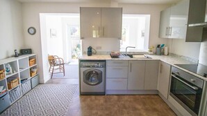 Eine moderne Küche mit Waschmaschine, Spüle und Herd. Ein Stuhl und ein Regal mit Körben sind ebenfalls vorhanden.
