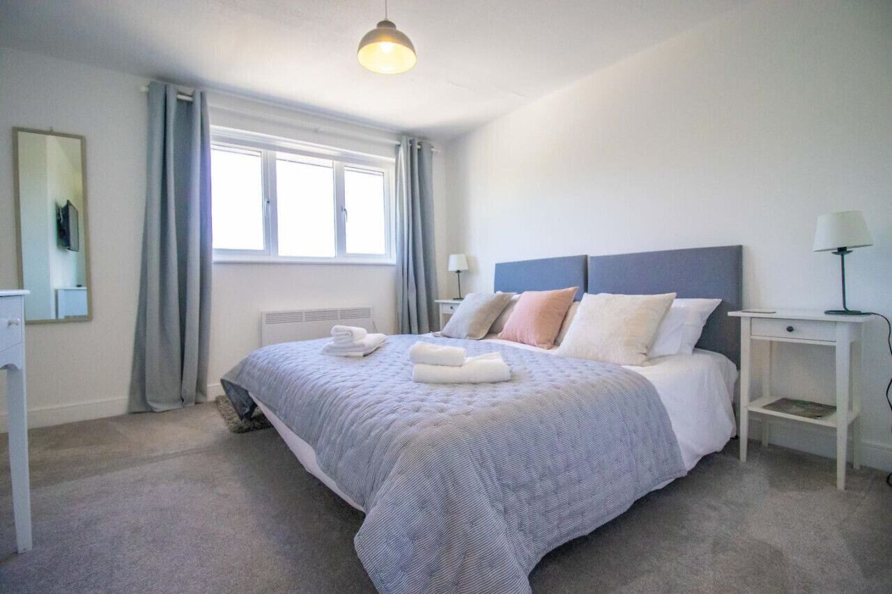 A neatly arranged bedroom with a large bed, a bedside table, a lamp, and a window with curtains.
