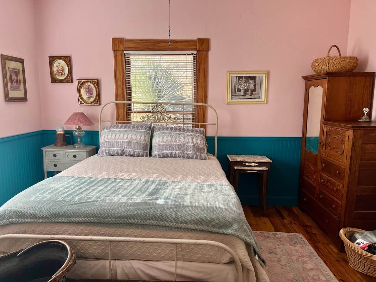 A bedroom with a bed, a nightstand, a dresser, and a window with blinds.
