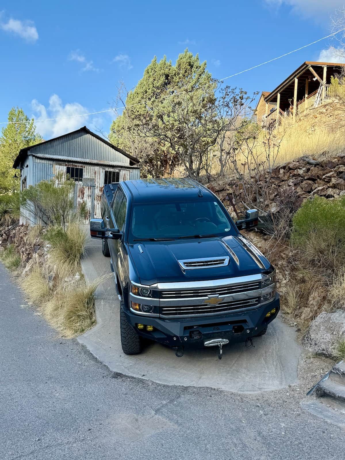 A blue truck parked on a narrow road beside a building with a corrugated metal roof.