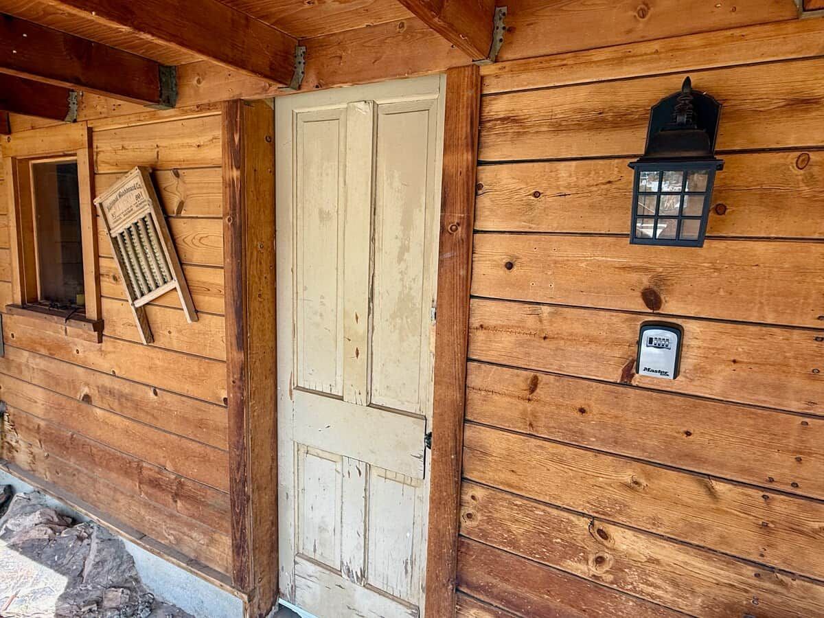 A wooden door with a window above it, a small window with a grate, and a wall-mounted lantern.