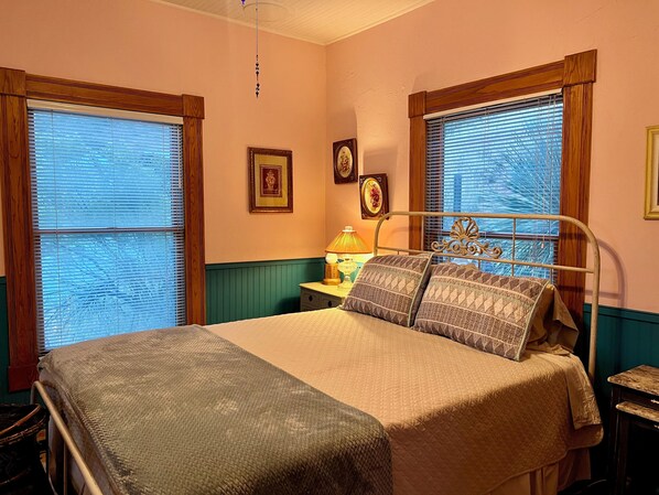 Un dormitorio con cama, mesita de noche, lámpara y cuadros en la pared.