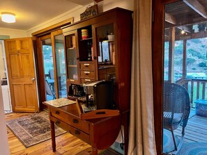 A wooden desk with a keyboard and a coffee maker, a cabinet with glass doors, and a view of a deck and outdoor area. - Top of the Stairs Old Bisbee|Park & Walk to Main Street (Bisbee)