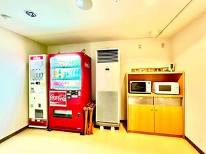 Una habitación con máquina expendedora, aire acondicionado y microondas sobre un mueble de madera.