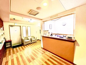 A reception area with a wooden floor, two armchairs, a reception desk with a clock, and a door in the background.