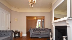 A living room with a grey sofa, a fireplace, and a chandelier. - Luxurious Victorian Home by the sea - Myana House (Lowestoft)