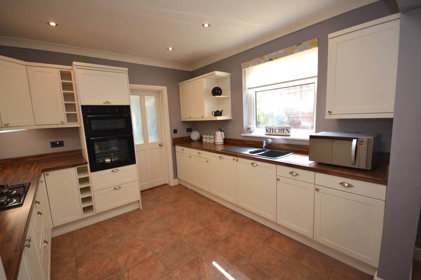 A compact kitchen with white cabinetry, a built-in oven, a microwave, and a window providing natural light.