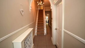 A hallway with a patterned floor, a staircase with a chandelier, and a door on the right. - Luxurious Victorian Home by the sea - Myana House (Lowestoft)