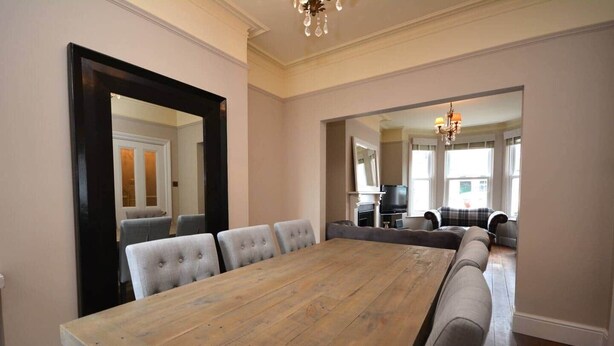 A spacious dining area with a large wooden table and grey upholstered chairs. - Luxurious Victorian Home by the sea - Myana House (Lowestoft)