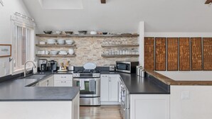 Eine moderne Küche mit Oberlichter, weißen Schränken, einer Ziegelrückwand und verschiedenen Geräten.