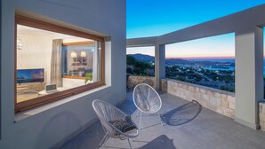 A modern balcony with two white chairs, a laptop on a small table, and a view of a cityscape at dusk. - Infinite Blue Apartments (Malevizi)