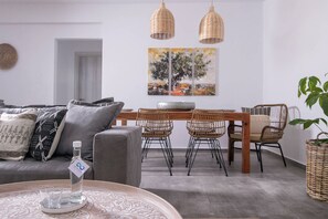 En moderne stue med en grå sofa, fletstole, et træspisebord og et stort maleri på væggen.