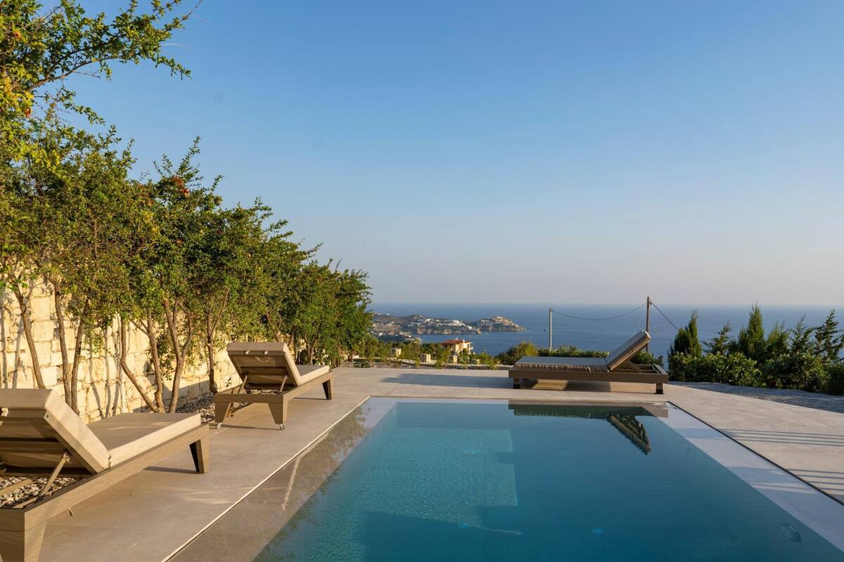 A pool area with lounge chairs and a view of the sea.