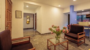 A lobby with a wooden door, a framed picture, a glass table with flowers, and a brown chair. - Bungalows San Felipe (Oaxaca)