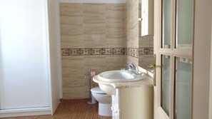 A compact bathroom with a white toilet and sink, featuring a decorative border and a gold-framed mirror.