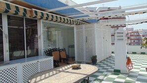 Relax on the patio with a round table and single chair, surrounded by lush greenery and a checkered floor.