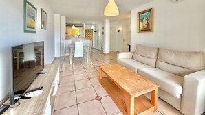 A modern living room with a TV, sofa, wooden coffee table, and a dining area with chairs and a table. - TERRASOL PALMA (Torre del Mar)