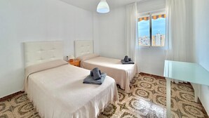 A hotel room with two beds, a small table, a window with curtains, and patterned floor tiles. - TERRASOL PALMA (Torre del Mar)