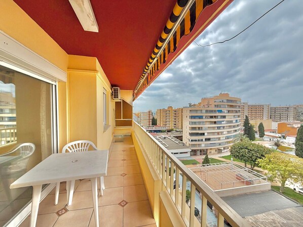 A balcony with a table and chairs, a red ceiling, and a view of surrounding buildings. - TERRASOL PALMA (Torre del Mar)