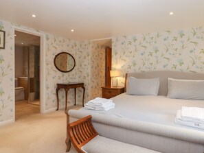 A hotel room with a bed, a chair, a nightstand, a lamp, and a bathroom visible through an open door. - Waterland Farmhouse (Holsworthy)